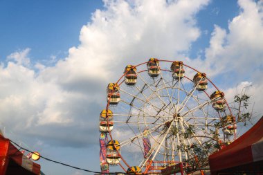 Arka planda renkli bir dönme dolap lunapark festivali gece pazarında açık mavi bir gökyüzü. Lunaparktaki dönme dolabı kapatın.