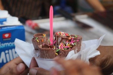 Çikolata karıştırılmış dondurma rulosu. Üstünde de elle yapılmış bir bardakta krema var. Bir kase rulo dondurmayı tutarken