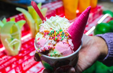 Çilekli ve vanilyalı dondurma üzerine çikolata parçacıkları serpilmiş. Dondurma külahı ve fincan.