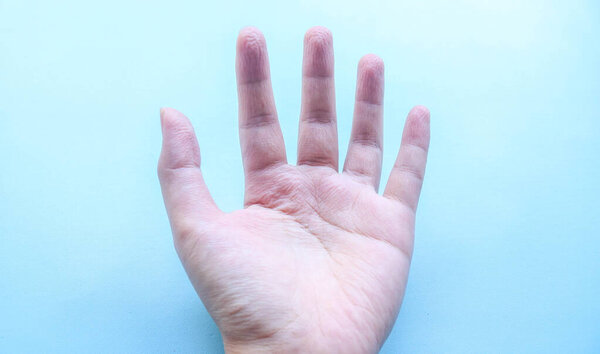 close up of a woman's wrinkled hands after playing in the water for a long time, cold hands become wrinkled isolated blue background