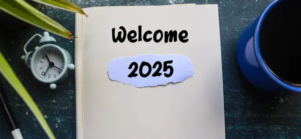 Defterde, ahşap masada alarmlı saat yazılı 2025 metni var. Yeni yıla hoşgeldiniz 2025