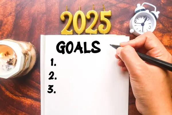 Bir insan aromaterapi mumları ve saatle çevrili bir deftere 2025 gol atar. Bir 2025 yapılacaklar listesi planlanıyor