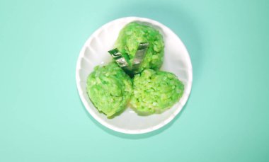 Yeşil arka planda izole edilmiş bir tabakta servis edilen yuvarlak şeklinde yeşil yapışkan pirinç bandı. Muz yapraklarına sarılı Endonezya yapışkan pirinç bandı