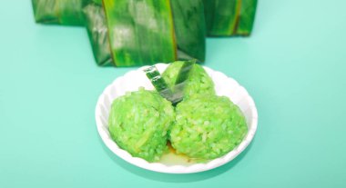 Yeşil arka planda izole edilmiş bir tabakta servis edilen yuvarlak şeklinde yeşil yapışkan pirinç bandı. Muz yapraklarına sarılı Endonezya yapışkan pirinç bandı