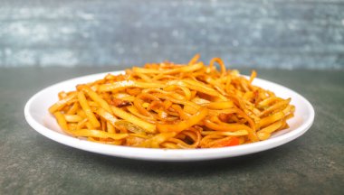 Baharatlı kızarmış şehriye, lahana, havuç ve gri arka planda beyaz bir tabakta kırmızı biber gibi sebzeler. Endonezya yemeği kızartılmış şehriye