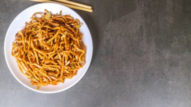 Baharatlı kızarmış şehriye, lahana, havuç ve gri arka planda beyaz bir tabakta kırmızı biber gibi sebzeler. Endonezya yemeği kızartılmış şehriye