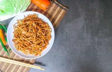 Baharatlı kızarmış şehriye, lahana, havuç ve gri arka planda beyaz bir tabakta kırmızı biber gibi sebzeler. Endonezya yemeği kızartılmış şehriye