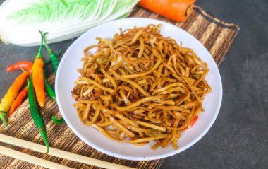 Baharatlı kızarmış şehriye, lahana, havuç ve gri arka planda beyaz bir tabakta kırmızı biber gibi sebzeler. Endonezya yemeği kızartılmış şehriye