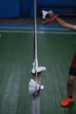 A badminton shuttlecock is caught in the net of the Jambi badminton court, with a blurred background of the players in action