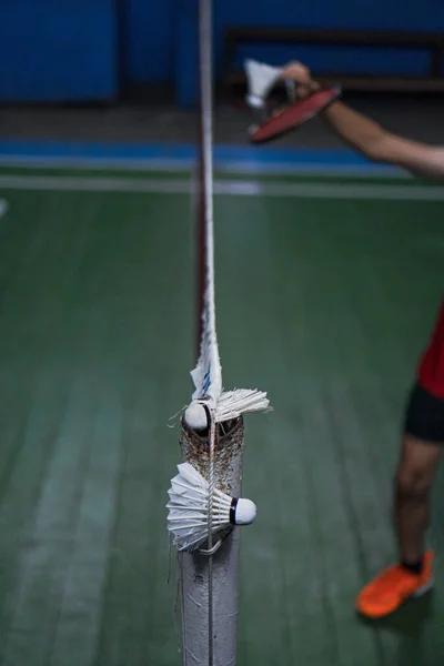 A badminton shuttlecock is caught in the net of the Jambi badminton court, with a blurred background of the players in action