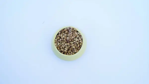 Beyaz arka planda izole edilmiş beyaz kasede kurumuş kişniş tohumlarının düz (üst görünümü) yatıyordu.