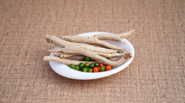Ashwagandha Dry Root with Fresh Green Leaves in a white Bowl, also known as Withania Somnifera, Ashwagandha, Indian Ginseng, Poison Gooseberry, or Winter Cherry. Kahverengi arkaplanda izole edilmiş.