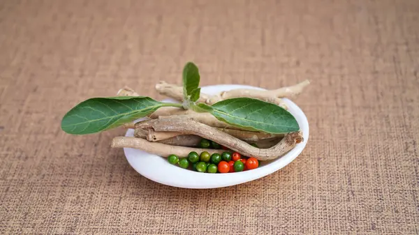 Ashwagandha Dry Root with Fresh Green Leaves in a white Bowl, also known as Withania Somnifera, Ashwagandha, Indian Ginseng, Poison Gooseberry, or Winter Cherry. Kahverengi arkaplanda izole edilmiş.