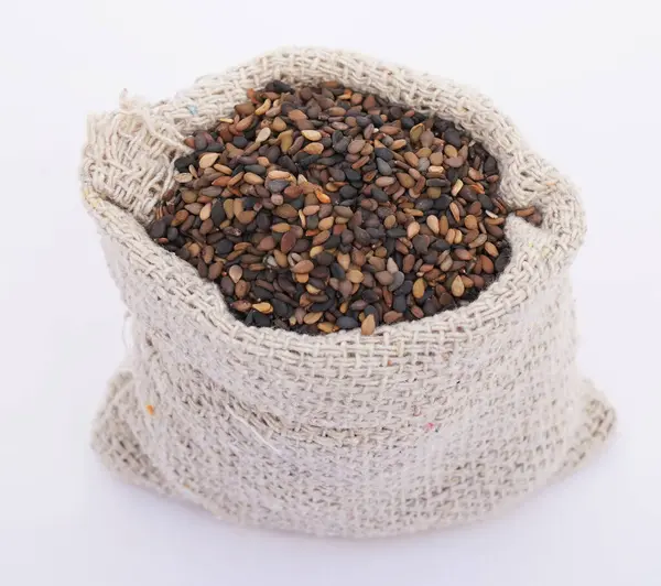Siyah Susam (Sesamum indicum) organik susam tohumlarının yakın plan görüntüsü, beyaz bir arkaplanda izole edilmiş siyah susam tohumları yığını üzerinde bir jüt torba içinde tohumlar.