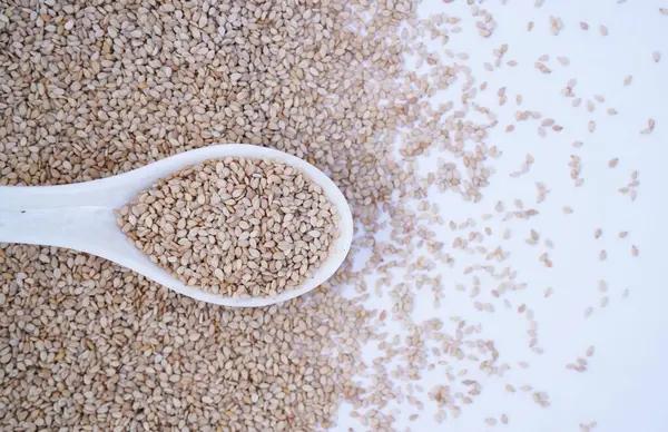 Organik Beyaz Susam tohumları (Sesamum indicum) ya da beyaz seramik çorba kaşığında kabuklu beyaz Til. Üst görünüm, kendi gradyan arkaplanı üzerinde.