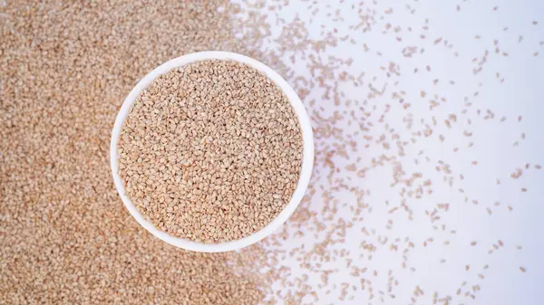 Beyaz Susam tohumu (Susamum indicum) ya da beyaz susam tohumlarının gradyan arka planına sahip beyaz seramik kasede kabuklu beyaz Til. Üst görünüm