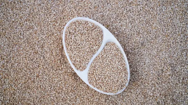 Raw sesame seeds in a wooden bowl and spoon over white til background. Organic benne grains for healthy food, boosting immunity diet and calcium source. Sesamum indicum crop. Asian cuisine. Top view.