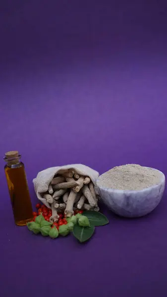 Ashwaganda Hint Ginseng tozu, yağ ve sopalar mor arka planda izole edilmiş.