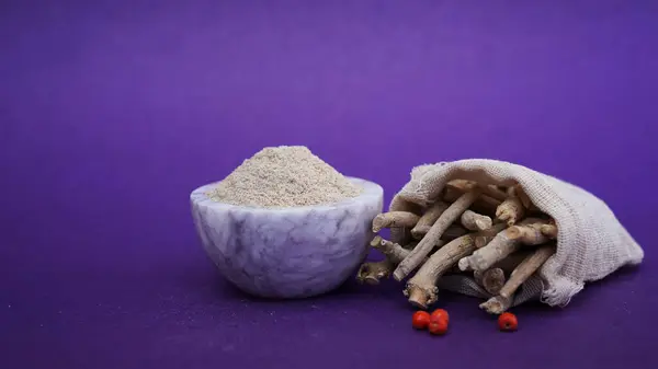 Ashwagandha Dry Root and powder also known as Withania Somnifera, Ashwagandha, Indian Ginseng, Poison Gooseberry, or Winter Cherry. Isolated on Purple Background.