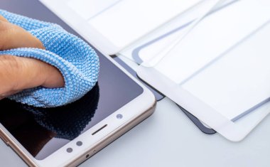 Bakım ve akıllı telefonları tamir etmek. El mavi peçeteyle telefon ekranını temizliyor. Bir sürü sertleştirilmiş cam ekran koruyucu. Mobil ekran koruyucusu. Koruyucu kapak filmi kurulumu