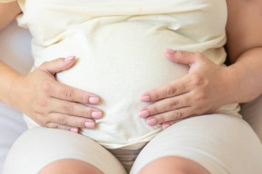 Hamile bir kadın yatakta. Karın bölgesinde. Düz bira hapları ve su ölçme bandıyla ya da elleri karnının üzerinde kalp şeklinde tutarak.