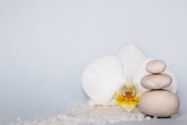 Spa sağIık kavramı. Piramit deniz tuzu ve orkide çiçeğindeki çakıl taşları gri kağıt arka planda izole edilmiş. Dalgalar gibi deniz tuzu.