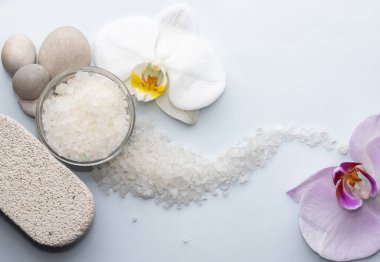 Spa sağIık kavramı. Piramit deniz tuzu ve orkide çiçeğindeki çakıl taşları gri kağıt arka planda izole edilmiş. Dalgalar gibi deniz tuzu.