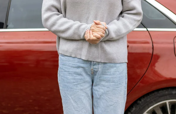 woman in front of lateral door red car in warm pullover blue jeans holding hands on waist,typing message smartphone,one leg raised up,sole of boot open door searching in vehicle interior back view.