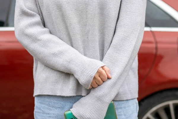 woman in front of lateral door red car in warm pullover blue jeans holding hands on waist,typing message smartphone,one leg raised up,sole of boot open door searching in vehicle interior back view.