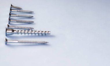 screw different sizes in a row and one is down, light blue background. Stainless bolt kid hand. Hardware repair tools isolated, free space for text, copy paste. be, think different, unique concept