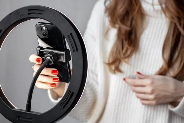 woman girl young blogger vlogger talking with followers hand holding phone in middle of selfie light round lamp.blonde hair red nails female explaining moving hands from side to side or typing 