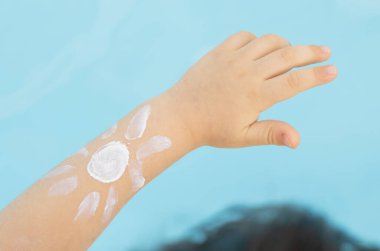 sun shape drawn from body spf uv protection cream lotion on teeneager girl or boy kid child hand shoulder against pool water.summer vacation red skin tan sun block cream