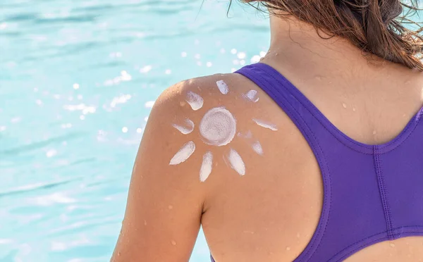 sun shape drawn from body spf uv protection cream lotion on teeneager girl or boy kid child hand shoulder against pool water.summer vacation red skin tan sun block cream