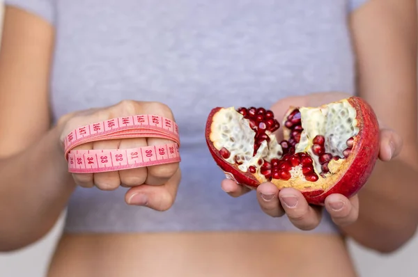 healthy food nutrition for getting fit slim body weight loss.woman girl female hands holding one apple or pomegranate fruit and measure tape around fist.post partum after child birth belly recovery