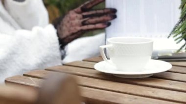 woman in white bathrobe outside sitting on chair drinking coffee from cup flip through magazine outside park coffee cafe shop.unrecognizable girl crazy outdoors typing message using smartphone