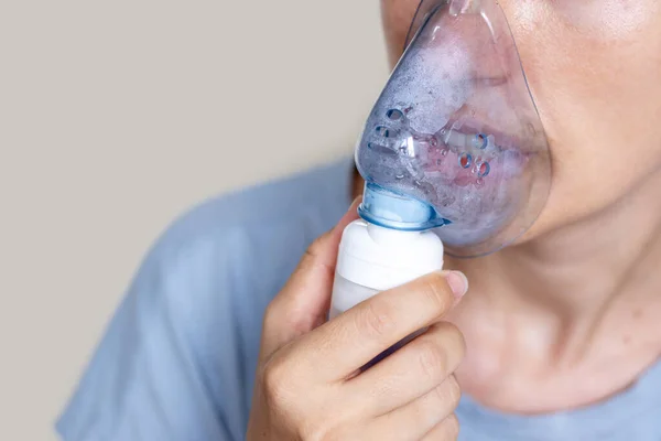 Solunum hastalıkları tedavi konsepti için sprey nebulizer kullanan kadın, fizyolojik çözüm tuzlu su. Bilinmeyen kadın izole ışık arka planı. Evde boş alan kopyalama macununda solunum.