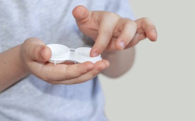 kid child little boy holding silicone contact lens on finger or trying to get out the lenses from case box.improve vision better with optical issue problem myopia.safety wearing isolated on beige back