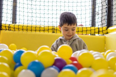 kid having fun in play center pool with colorful many balls.happy smiling child preschooler boy throwing tossing up plastic balls playground interior inside mall.soft ocean plastic balls cover face