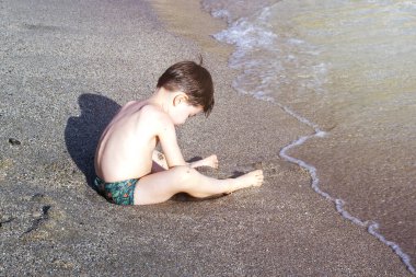 kid playing on beach sand running digging using plastic toys crab lobster seahorse shell shape rake and sprinkler.sunny summer vacation day child preschooler boy feet legs in water waves