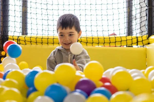 kid having fun in play center pool with colorful many balls.happy smiling child preschooler boy throwing tossing up plastic balls playground interior inside mall.soft ocean plastic balls cover face