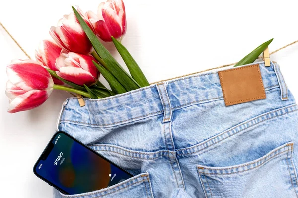 tulips on jeans and spring calling on smartphone.slide to answer incoming call.kid holding bouquet of flowers wrapped in paper on window sill.easter holiday origami rabbit mother women day march 8th
