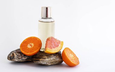 small shower gel or shampoo bottle with golden color liquid isolated with grapefruit and tangerine half fruits slice on solid rock stone.product in soap holder with shower exfoliating sponge orange