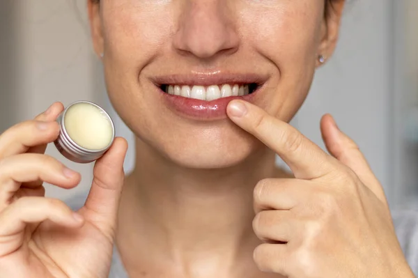 woman applying on lips balm or scrub from natural ingredients half bottom face kissing gesture smiling female.scrub and lip balm from small jars girl taking with finger rotation moves coconut oil