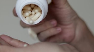 Kadın plastik kabarcıktan ya da beyaz şişe haplarından kapsül balık yağı haplarından birini alıp palmiyeye döker. Bir adet yuvarlak kalsiyum hapı. Kadınları parmaklarıyla yuvarlar. Yiyecek takviyesi vitaminleriyle oynar.