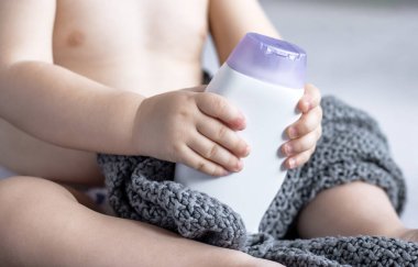 Bebek şampuan banyosu jeli şişesi yumuşak oyuncak ayı reklam afişi reklamları. Bebek bebek yatakta oyun oynuyor. Portre çocuğu elleriyle kafa boşluğunda komik yüz ifadeleri yapıyor.