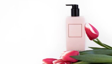 Üzerinde pembe ya da gri arka planda izole lale çiçekleri olan boş bir alan için çerçeveli pembe şişe. Kozmetik şişe vücut bakım kremi losyonu. Çiçekler tekstil kırmızısı koyu renkli materyal. Dizüstü bilgisayar.