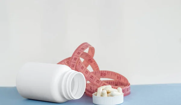 Steteskoplu C vitamini kapsüllü beyaz haplar şişesi ve ölçüm bandı. Zayıflık konseptine uygun sağlıklı besin takviyeleri.