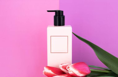 Üzerinde pembe ya da gri arka planda izole lale çiçekleri olan boş bir alan için çerçeveli pembe şişe. Kozmetik şişe vücut bakım kremi losyonu. Çiçekler tekstil kırmızısı koyu renkli materyal. Dizüstü bilgisayar.