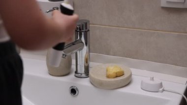 Çocuk banyoda dişlerini elektrikle yıkıyor aynaya bakıyor ve gülümsüyor. Sevimli anaokulu lavaboda doğal biyo-organik sabun takviyesiyle ellerini yıkıyor.