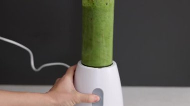 Kadın mutfakta kereviz, elma, mandalina, kivi ve ıspanak karışımından sağlıklı bir içecek hazırlıyor. Spor takım elbiseli kız blender kabında meyve, su ve karışım ekliyor. Kadın ezilmiş meyve, ince vücut 4k.